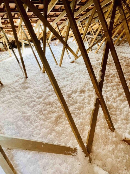 Ático con vigas de madera y aislante blanco en el suelo.